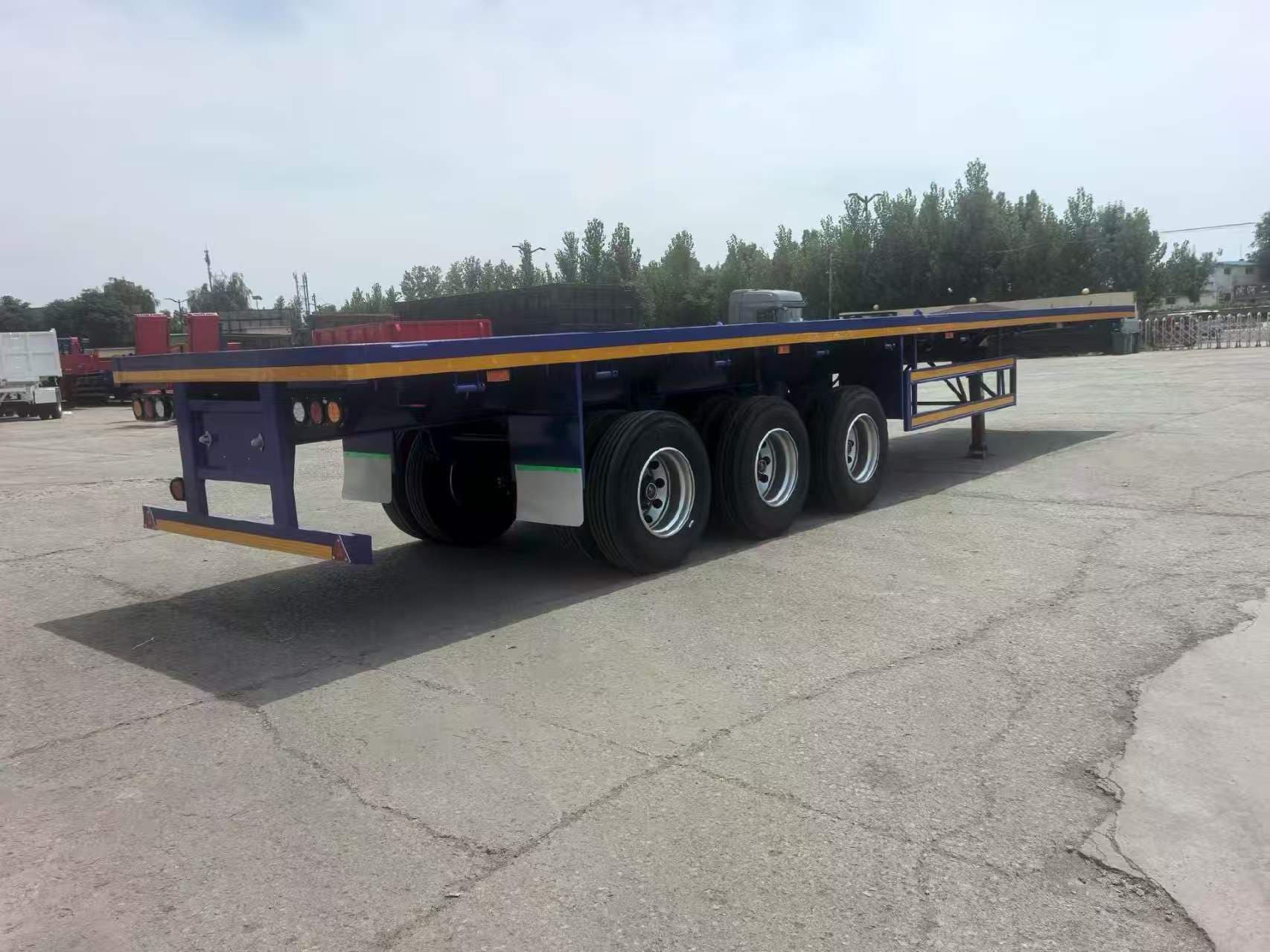 Blue three-axle flatbed trailer photographed in a supplier yard